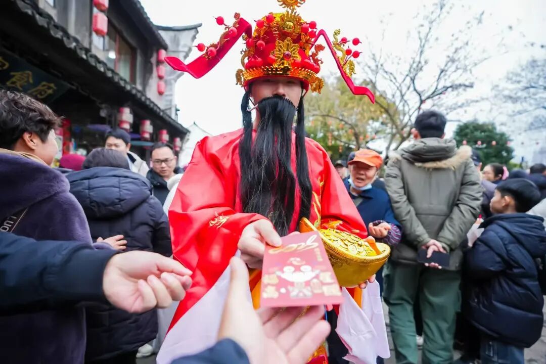 An actor portraying the God of Wealth passes out red envelopes to visitors..jpg
