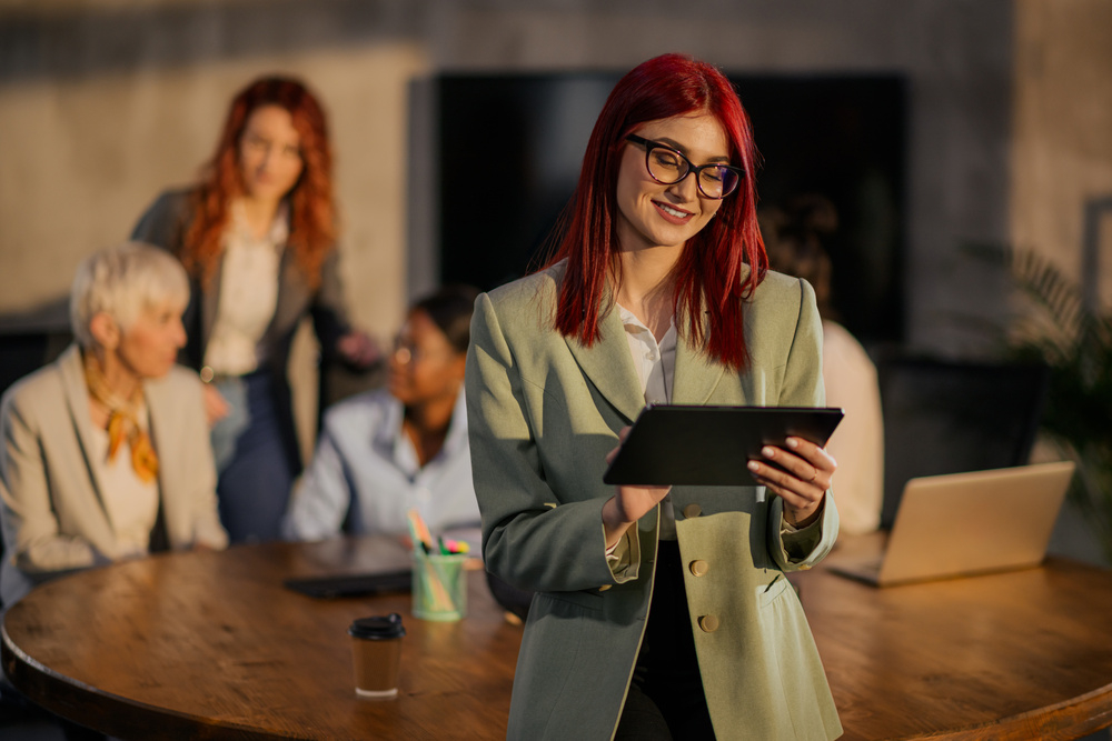就业素材-女企业家站在办公室里，对着平板电脑微笑.jpeg