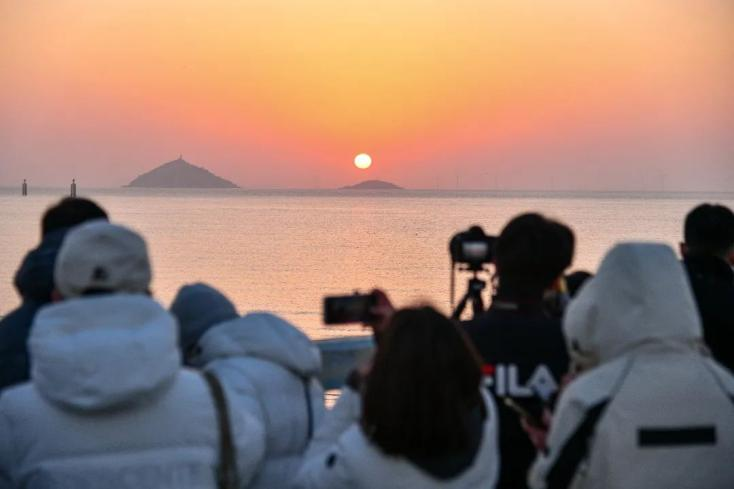 Visitors capture images of the sunrise over mountains at Jinshan City Beach..png